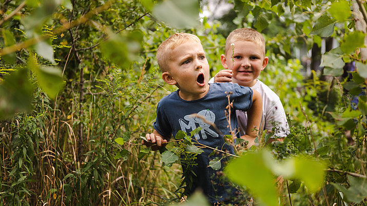 Zwei Jungs gehen in den Büschen im Naturerfahrungsraum im Park am Gleisdreieck auf Entdeckungstour